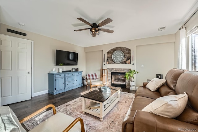 living room with dark hardwood / wood-style flooring, ceiling fan, and a stone fireplace