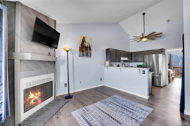 interior space featuring freestanding refrigerator, a large fireplace, a peninsula, wood finished floors, and under cabinet range hood