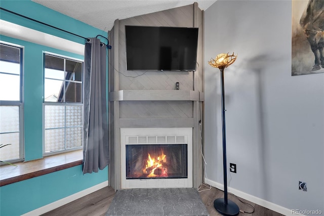 unfurnished living room featuring a large fireplace, a textured ceiling, wood finished floors, and baseboards