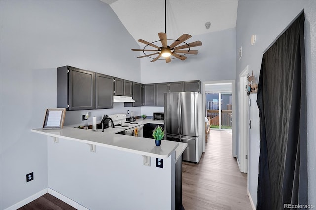 kitchen featuring under cabinet range hood, white electric range, a peninsula, light countertops, and freestanding refrigerator