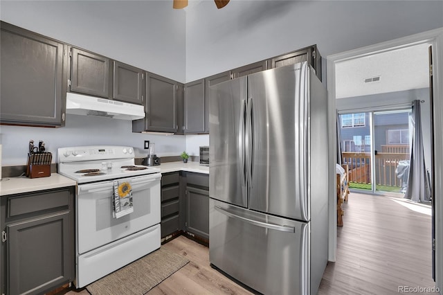 kitchen featuring white electric range oven, light countertops, light wood-style flooring, freestanding refrigerator, and under cabinet range hood