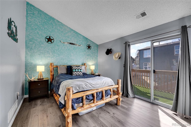 bedroom featuring access to outside, an accent wall, visible vents, and wood finished floors