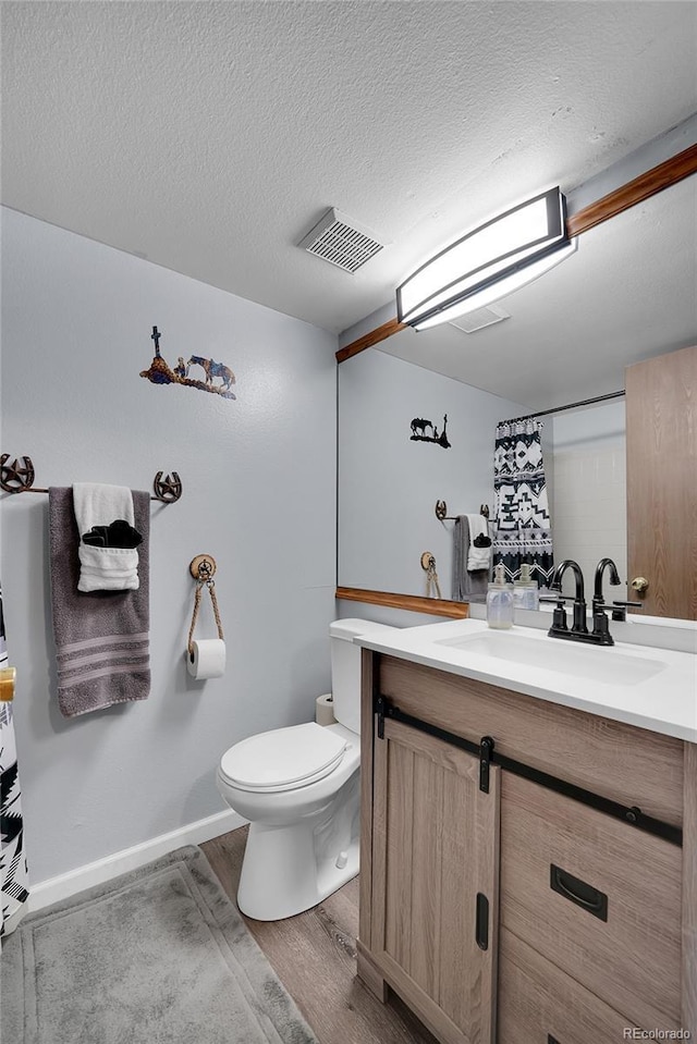 bathroom with visible vents, toilet, wood finished floors, a textured ceiling, and vanity