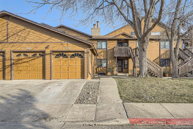 view of property featuring stairs, a chimney, a garage, and concrete driveway