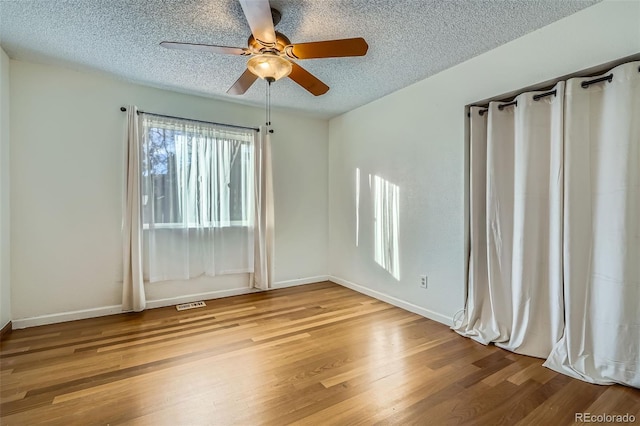 empty room featuring baseboards, a textured ceiling, visible vents, a ceiling fan, and wood finished floors