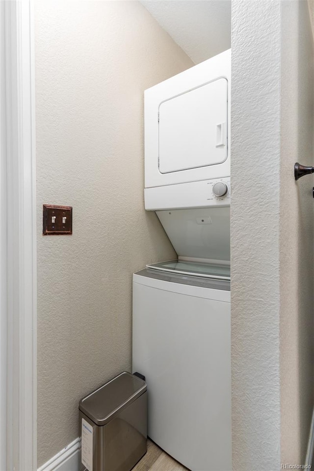 clothes washing area featuring stacked washing maching and dryer, laundry area, light wood-type flooring, and a textured wall