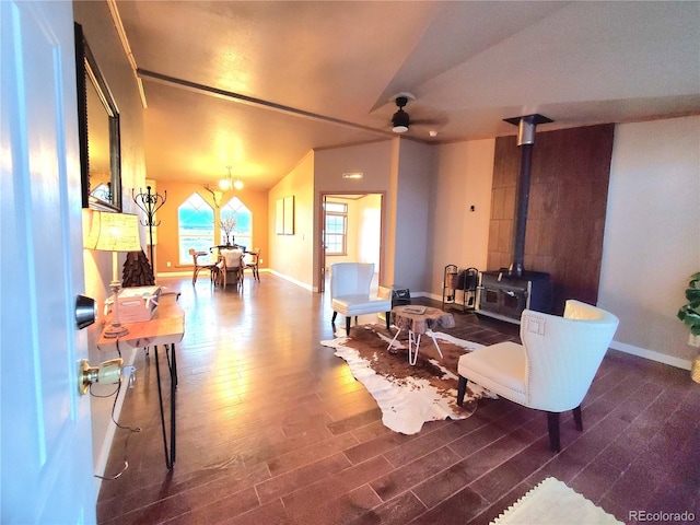 living room featuring vaulted ceiling, a wood stove, dark wood-type flooring, and ceiling fan with notable chandelier