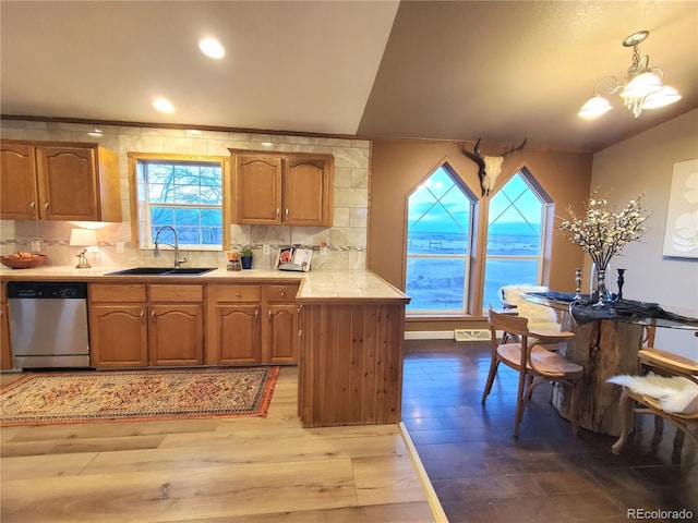 kitchen with backsplash, sink, hanging light fixtures, stainless steel dishwasher, and wood-type flooring