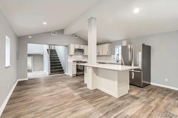 825 S Quitman St, Denver, CO 80219 - kitchen with freestanding refrigerator, stove, a kitchen island, white cabinets, and decorative backsplash