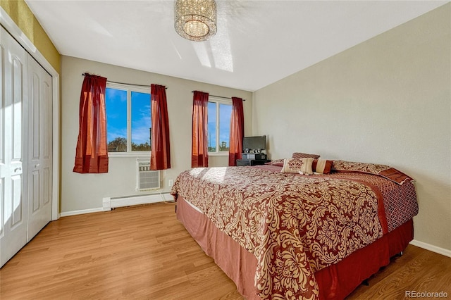 bedroom featuring a wall mounted AC, a closet, light wood-type flooring, and a baseboard heating unit