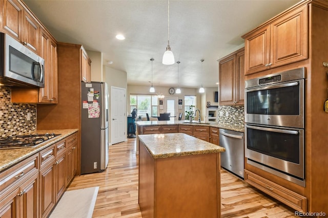 kitchen with kitchen peninsula, appliances with stainless steel finishes, sink, decorative light fixtures, and a center island