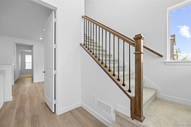 stairs with a wealth of natural light, visible vents, baseboards, and wood finished floors