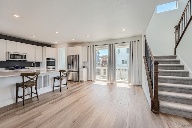 kitchen with a breakfast bar area, light wood-type flooring, light countertops, appliances with stainless steel finishes, and white cabinets