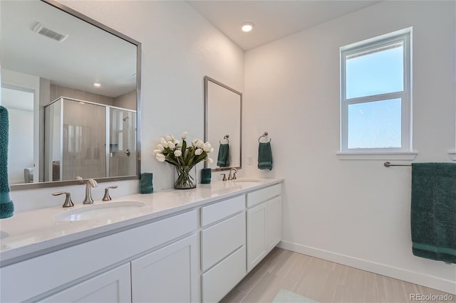 bathroom featuring visible vents, baseboards, double vanity, a stall shower, and a sink