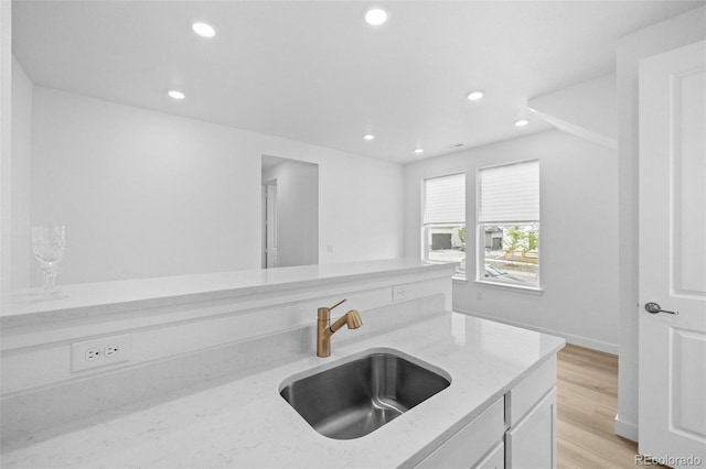 kitchen with light stone counters, light wood finished floors, recessed lighting, a sink, and white cabinetry