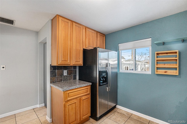 kitchen with tasteful backsplash, stone countertops, stainless steel fridge, and light tile patterned floors