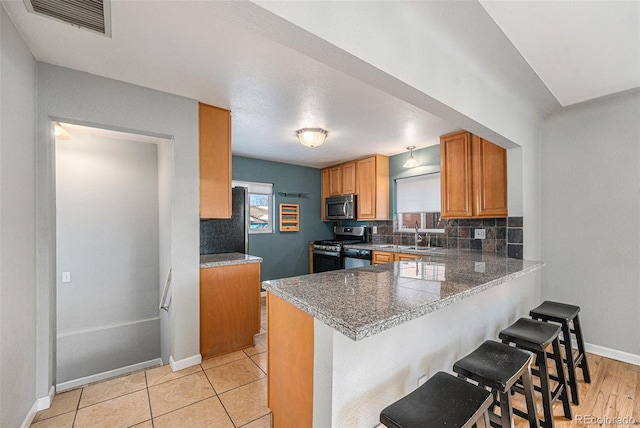 kitchen with a breakfast bar area, appliances with stainless steel finishes, tasteful backsplash, light tile patterned flooring, and kitchen peninsula