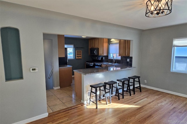 kitchen with sink, a kitchen breakfast bar, range with electric cooktop, a wealth of natural light, and kitchen peninsula