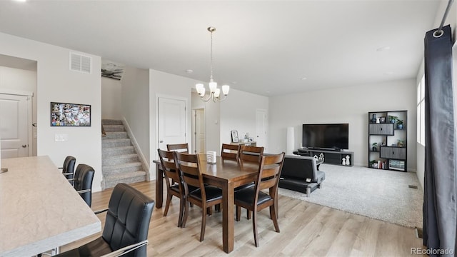 dining space featuring stairs, a notable chandelier, light wood finished floors, and visible vents