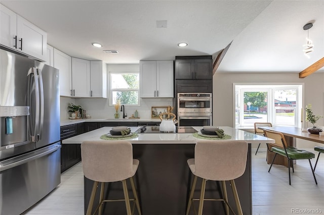 5195 Allison St, Arvada, CO 80002 - kitchen featuring appliances with stainless steel finishes, a kitchen breakfast bar, backsplash, white cabinets, and recessed lighting