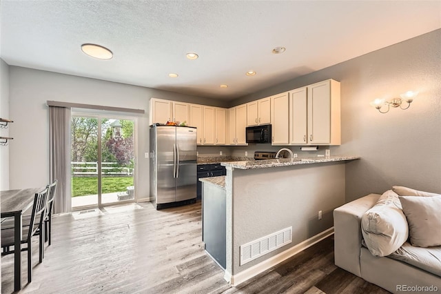 23882 E Alabama Dr, Aurora, CO 80018 - kitchen with freestanding refrigerator, black microwave, light wood-style floors, a peninsula, and light stone counters