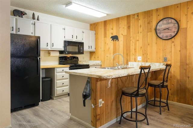 kitchen with white cabinets, a textured ceiling, wood walls, and black appliances