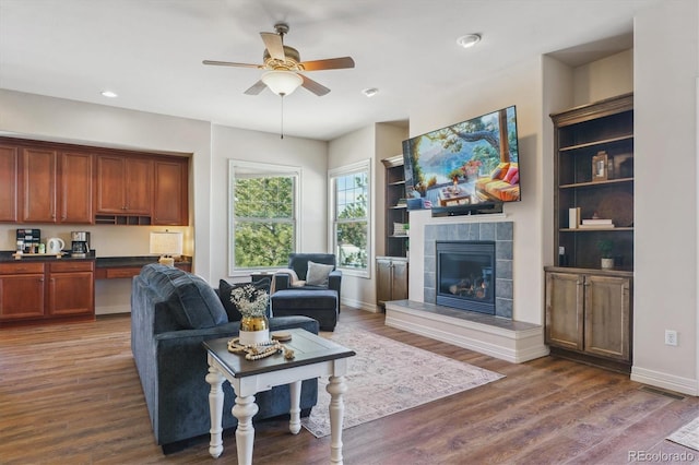 living room with ceiling fan, dark hardwood / wood-style floors, built in desk, and a tile fireplace