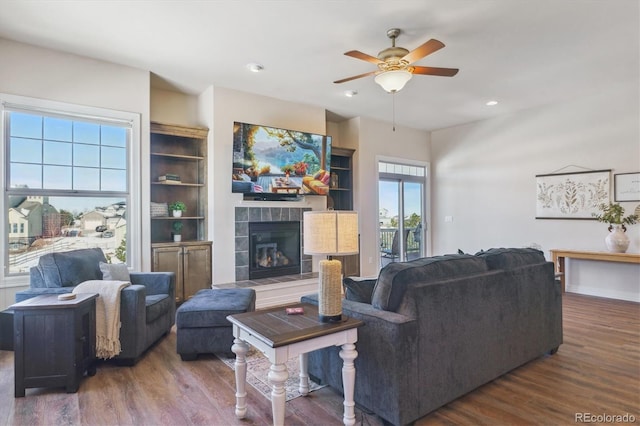 living room featuring dark hardwood / wood-style flooring, a tiled fireplace, and ceiling fan