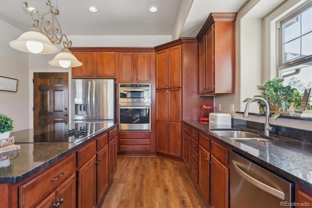 kitchen featuring sink, wood-type flooring, hanging light fixtures, dark stone countertops, and appliances with stainless steel finishes