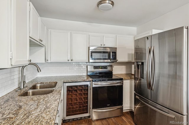 kitchen featuring stainless steel appliances, beverage cooler, a sink, light stone counters, and white cabinets