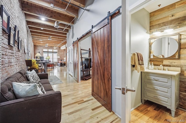 hall with brick wall, beamed ceiling, light hardwood / wood-style floors, sink, and a barn door