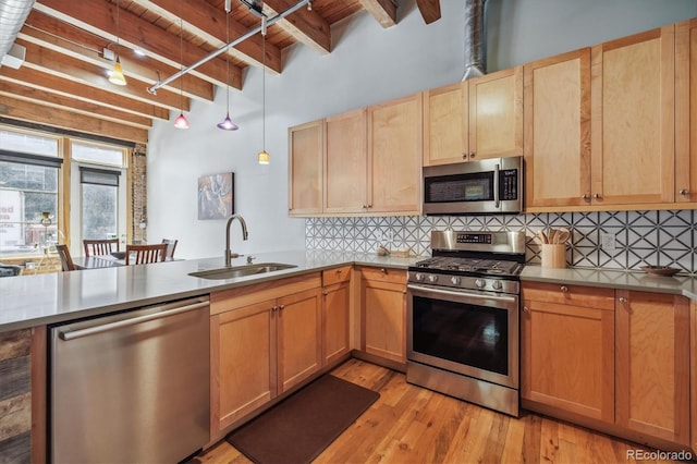 kitchen with appliances with stainless steel finishes, hanging light fixtures, sink, light wood-type flooring, and kitchen peninsula