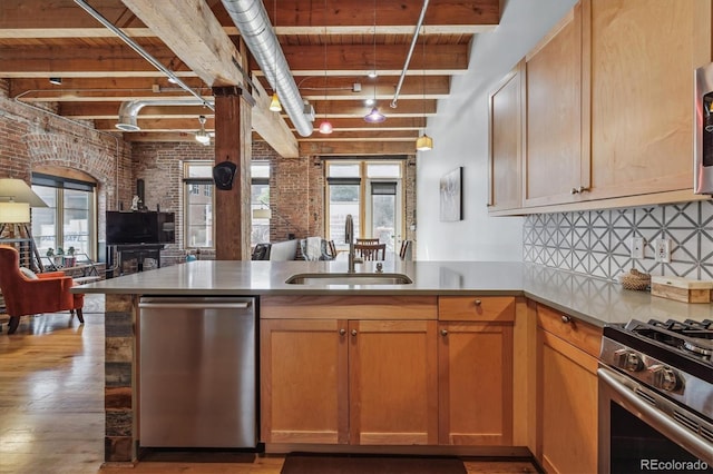 kitchen featuring kitchen peninsula, appliances with stainless steel finishes, sink, beam ceiling, and brick wall