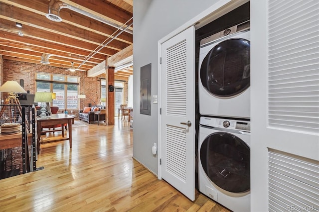 washroom featuring light hardwood / wood-style floors, electric panel, brick wall, and stacked washing maching and dryer