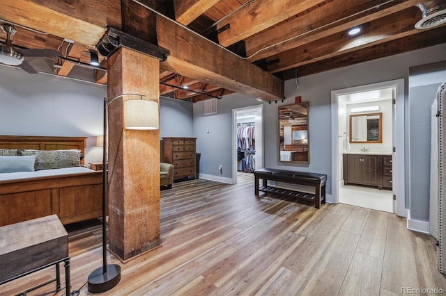 bedroom featuring a walk in closet, a closet, hardwood / wood-style flooring, ensuite bathroom, and beam ceiling