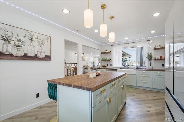 kitchen featuring a center island, sink, hanging light fixtures, butcher block countertops, and light hardwood / wood-style flooring