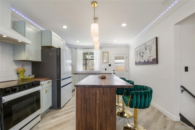 kitchen with butcher block countertops, electric stove, wall chimney exhaust hood, light hardwood / wood-style flooring, and a center island