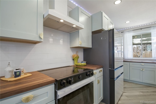 kitchen with black range with electric cooktop, light hardwood / wood-style floors, range hood, and wood counters