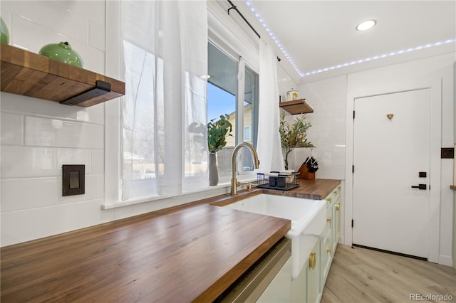 kitchen with stainless steel dishwasher, light hardwood / wood-style floors, wooden counters, and sink