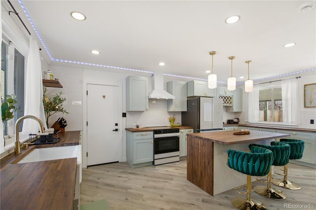 kitchen featuring wooden counters, premium range hood, fridge, sink, and range with electric cooktop