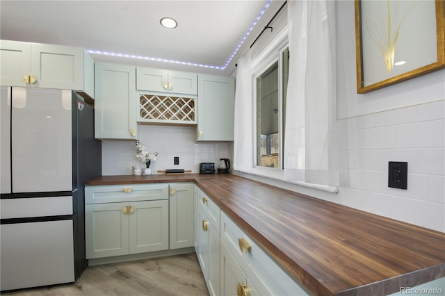 kitchen with decorative backsplash, wooden counters, refrigerator, and light hardwood / wood-style flooring