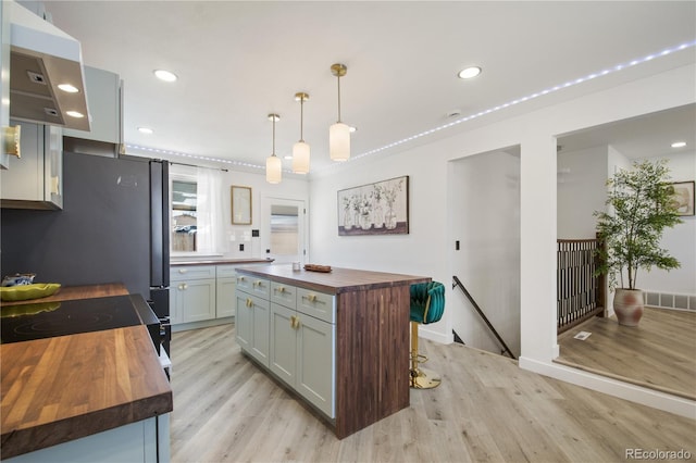 kitchen with a center island, pendant lighting, light hardwood / wood-style flooring, stainless steel fridge, and butcher block counters