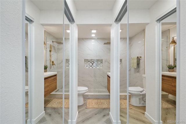 bathroom with toilet, tiled shower, hardwood / wood-style floors, and vanity