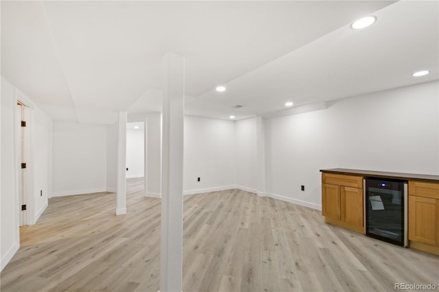 basement with bar, light hardwood / wood-style floors, and beverage cooler