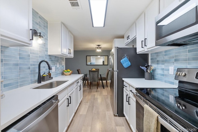 kitchen featuring visible vents, a sink, appliances with stainless steel finishes, light wood finished floors, and light countertops