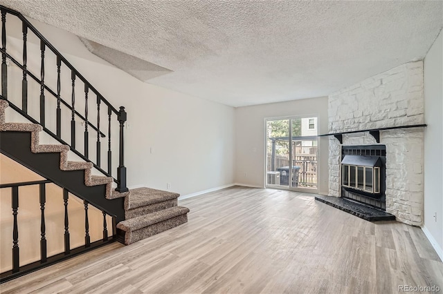 unfurnished living room featuring a stone fireplace, a textured ceiling, and light hardwood / wood-style flooring