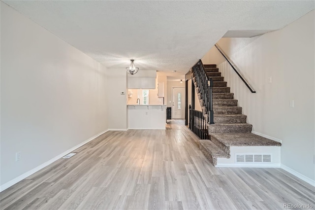 unfurnished living room with sink, a textured ceiling, and light hardwood / wood-style flooring