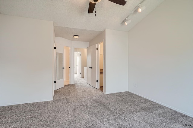 carpeted spare room with ceiling fan, track lighting, and a textured ceiling