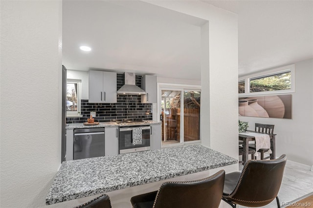 kitchen with kitchen peninsula, oven, wall chimney range hood, stainless steel dishwasher, and tasteful backsplash