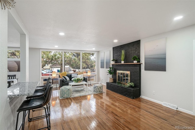 living room with a brick fireplace, a textured ceiling, wood-type flooring, and a healthy amount of sunlight